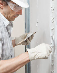 Albañil usando cuchara para aplicar el cemento blanco como recubrimiento de una pared