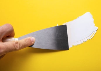 Cemento plástico siendo aplicado con espátula sobre fondo amarillo