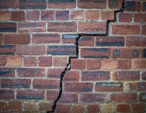 Un grieta vertical en medio de un muro hecho con ladrillos - grietas en muros